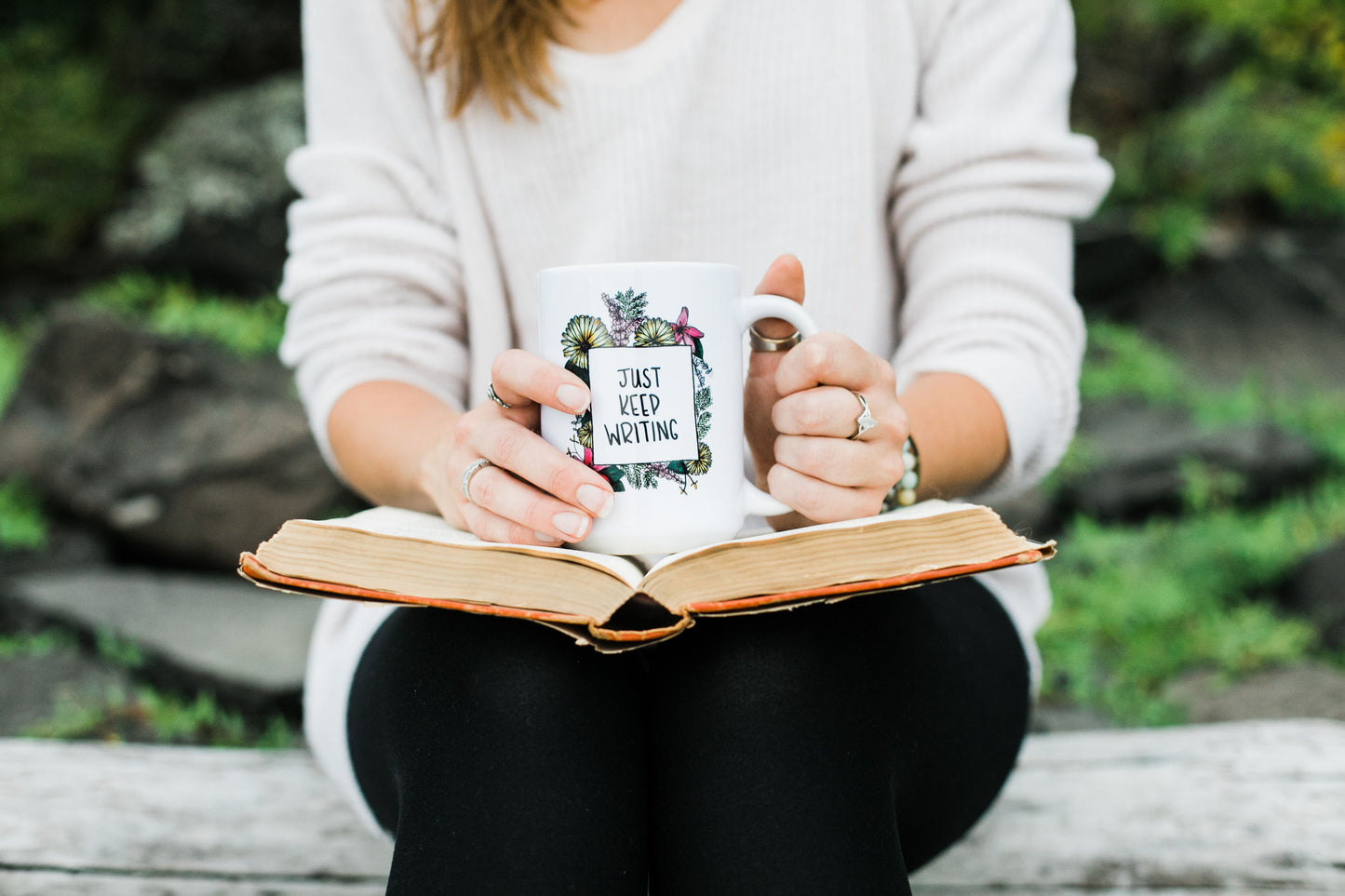 A white ceramic mug for writers. Text within a floral illustrated frame reads "Just Keep Writing"
