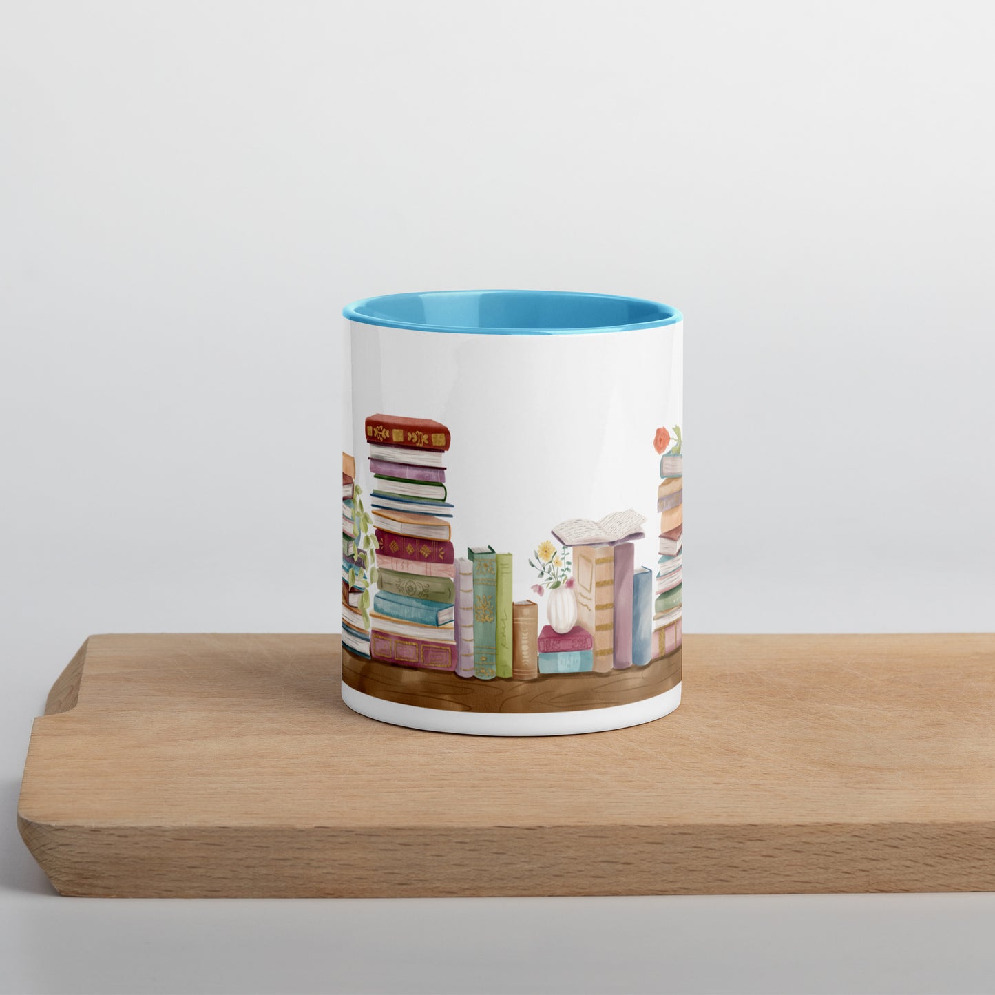A coffee mug for book lovers featuring a watercolor bookshelf design all around on white ceramic. The interior is a bright blue ceramic.