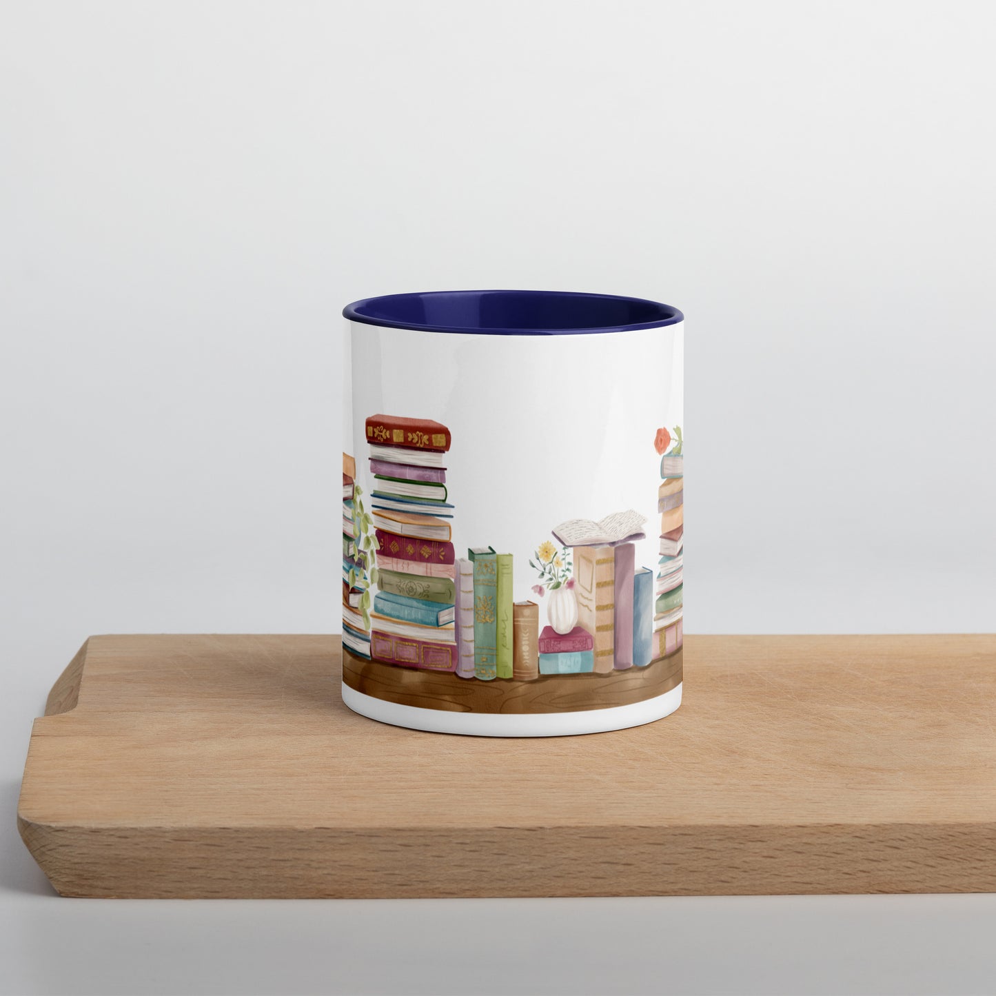 A coffee mug for book lovers featuring a watercolor bookshelf design all around on white ceramic. The interior is a dark blue ceramic.