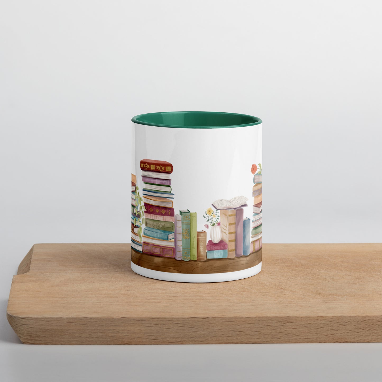 A coffee mug for book lovers featuring a watercolor bookshelf design all around on white ceramic. The interior is a dark green ceramic.