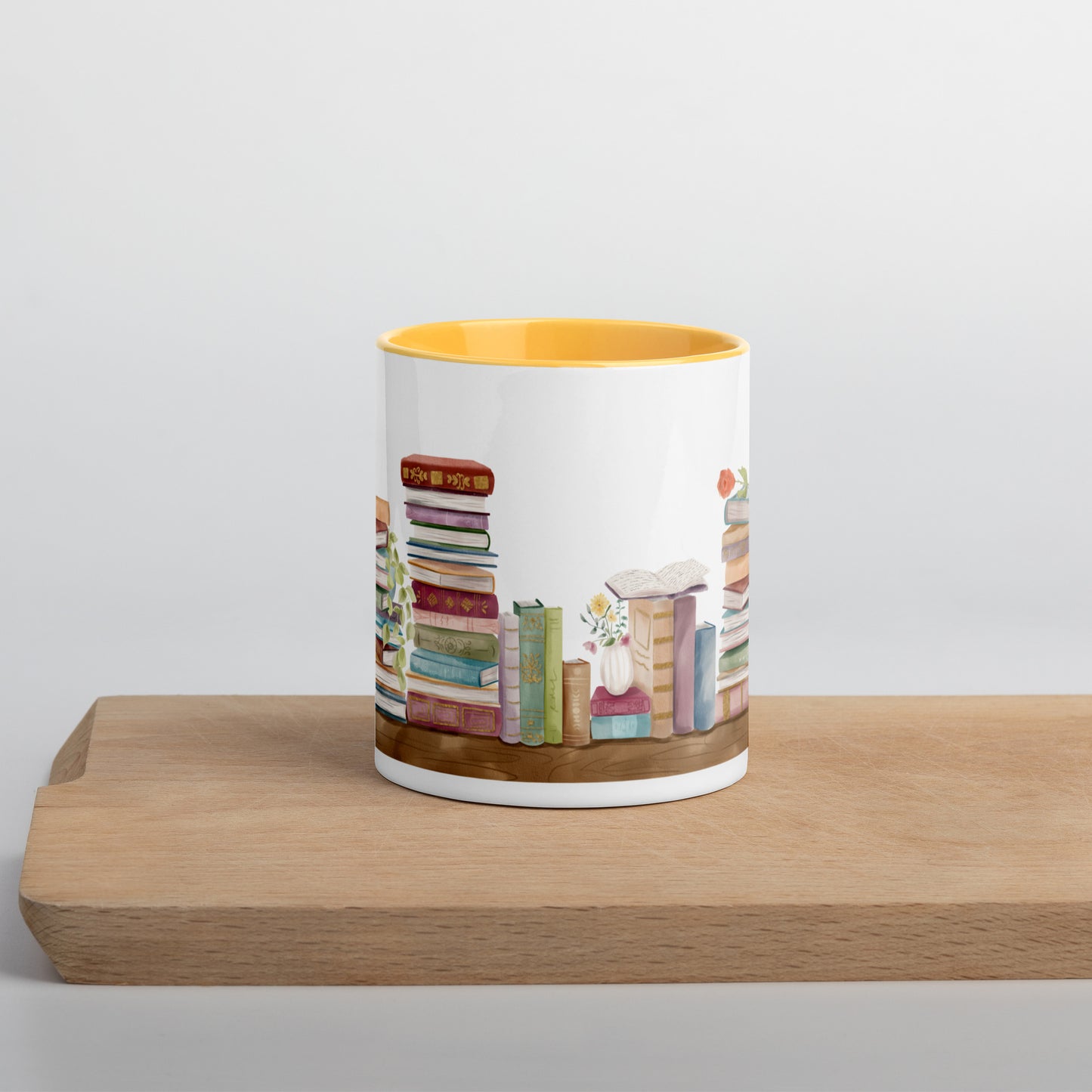 A coffee mug for book lovers featuring a watercolor bookshelf design all around on white ceramic. The interior is a golden yellow ceramic.