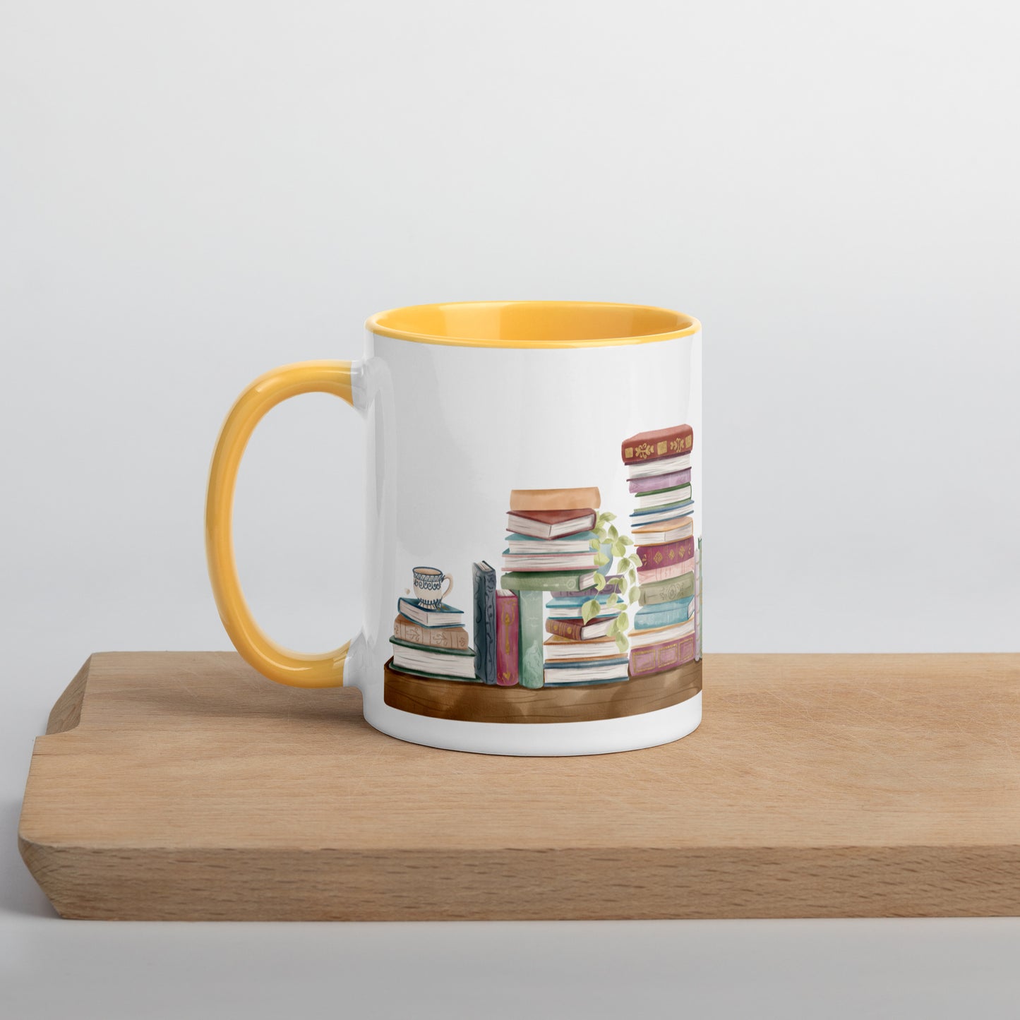 A coffee mug for book lovers featuring a watercolor bookshelf design all around on white ceramic. The interior is a golden yellow ceramic.