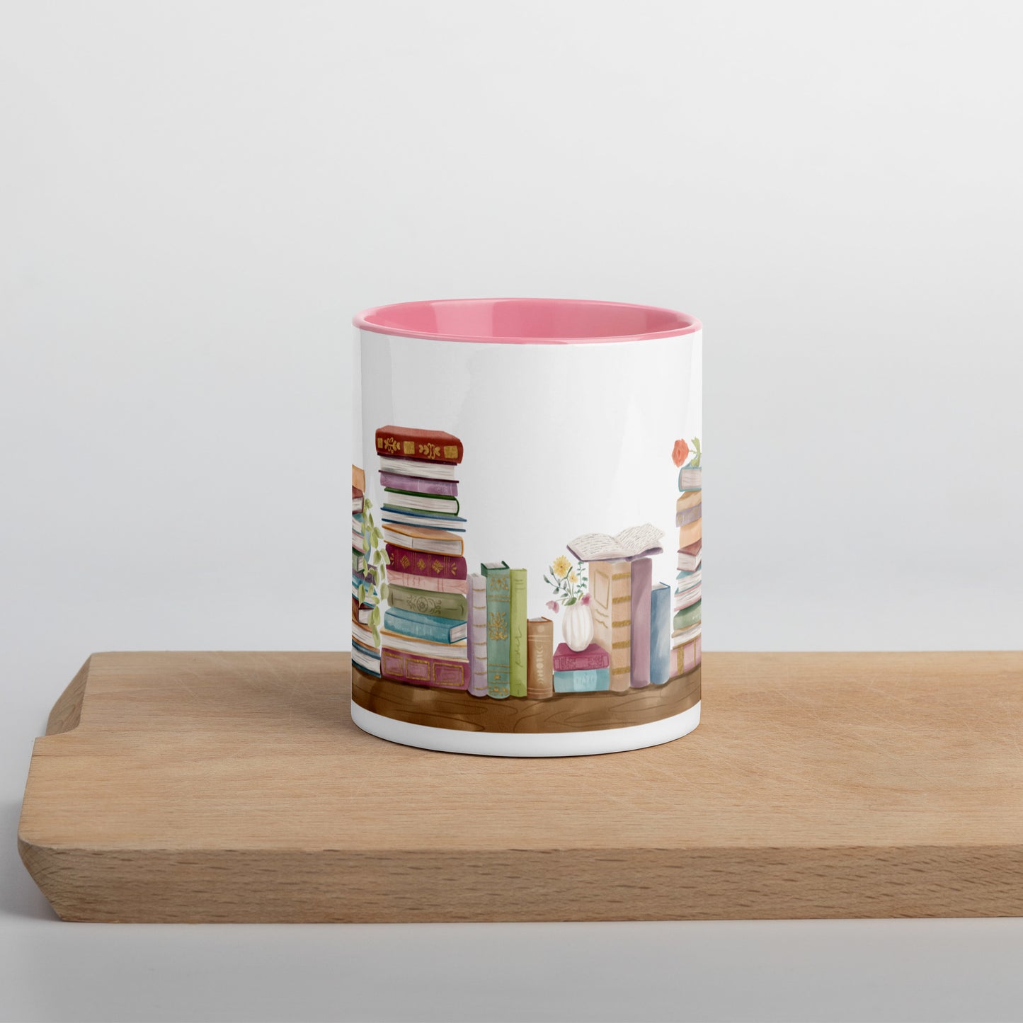 A coffee mug for book lovers featuring a watercolor bookshelf design all around on white ceramic. The interior is a soft pink ceramic.