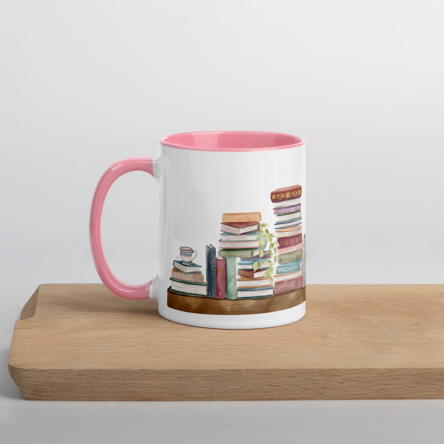 A coffee mug for book lovers featuring a watercolor bookshelf design all around on white ceramic. The interior is a soft pink ceramic.