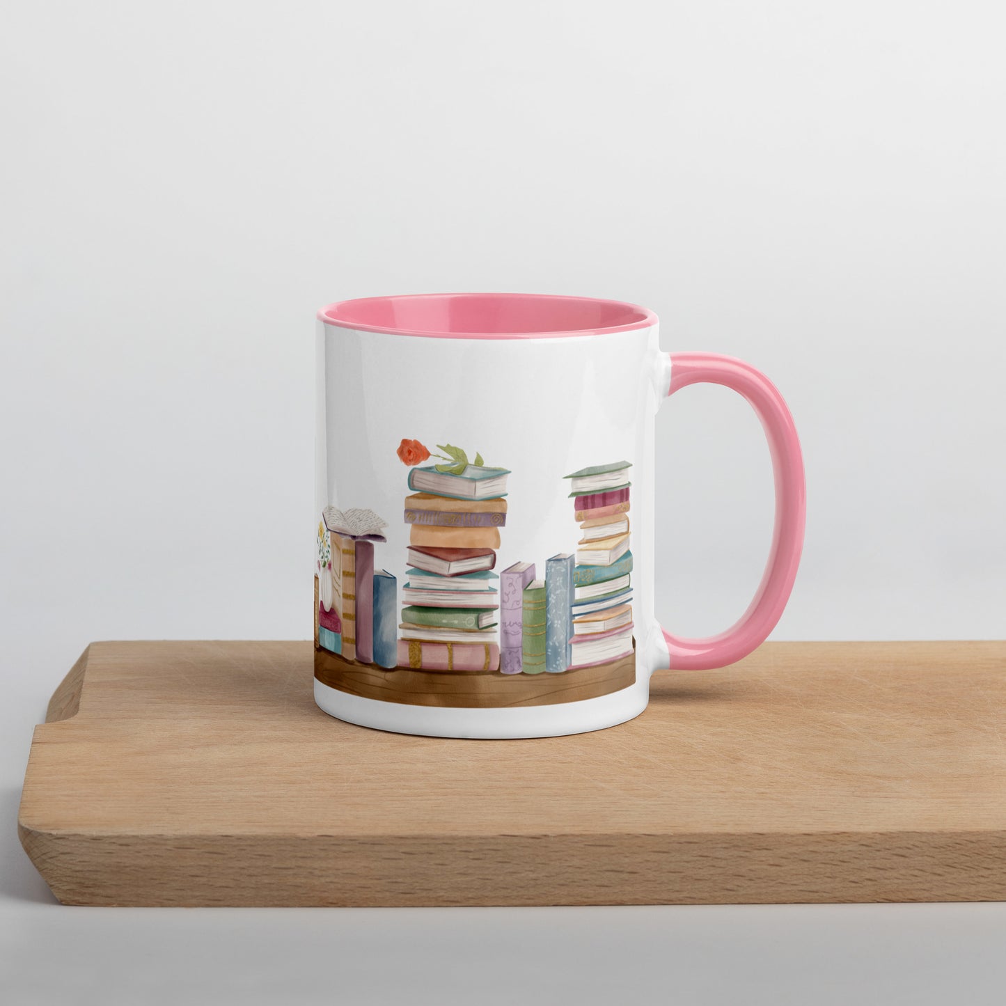A coffee mug for book lovers featuring a watercolor bookshelf design all around on white ceramic. The interior is a soft pink ceramic.