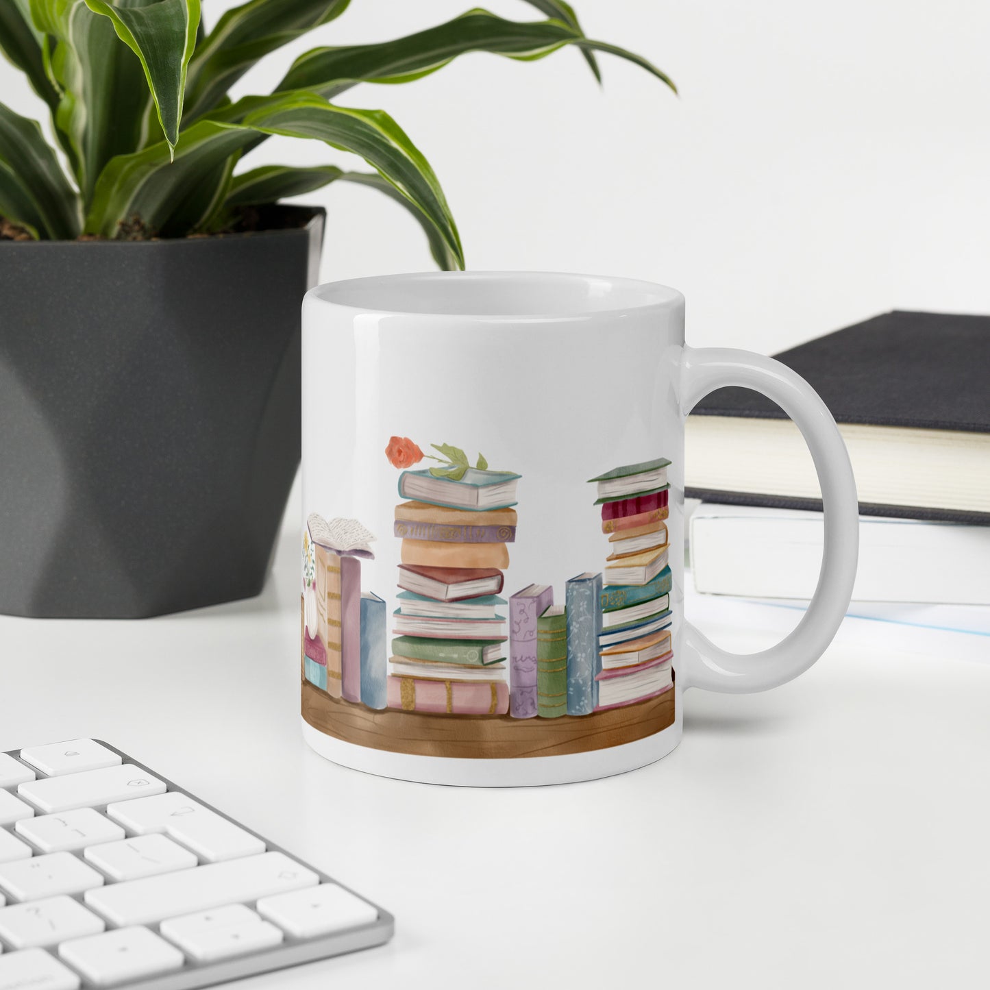 A white ceramic mug for book lovers featuring a wrap around design with stacks of watercolor illustrated books along a shelf.