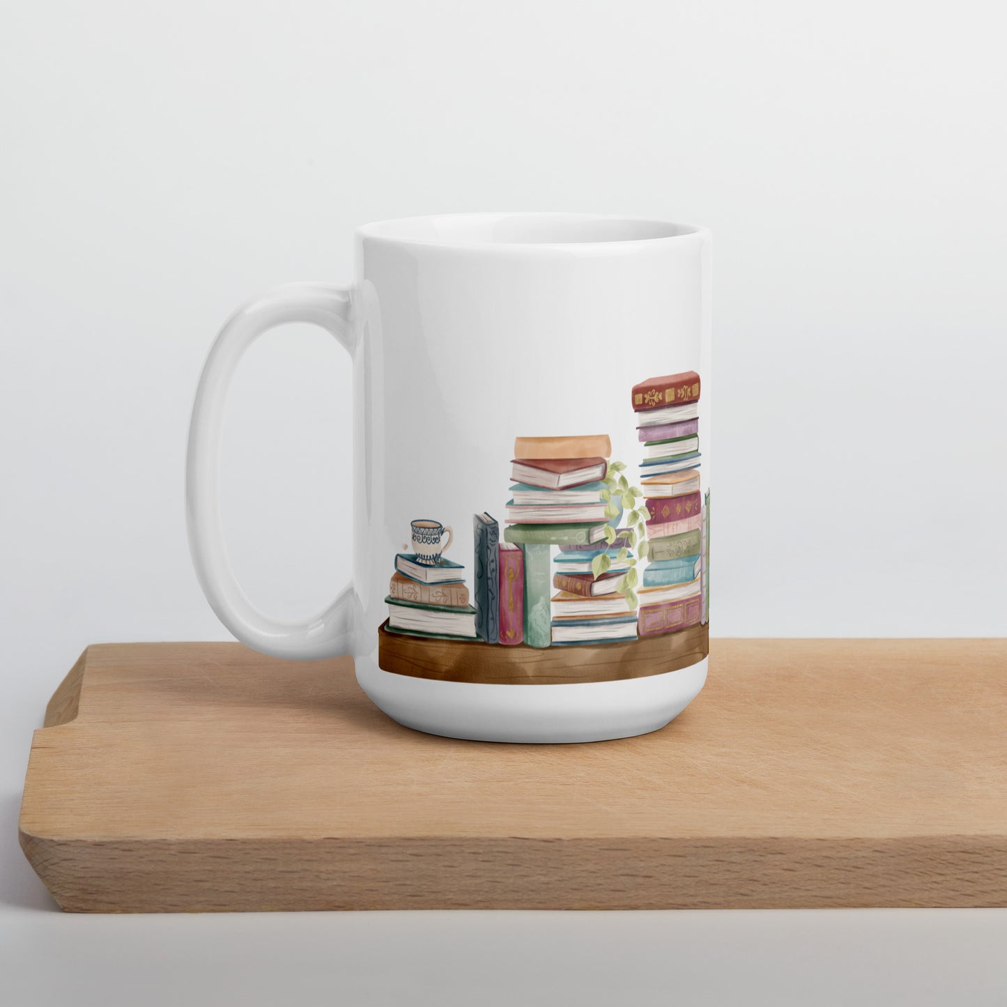 A white ceramic mug for book lovers featuring a wrap around design with stacks of watercolor illustrated books along a shelf.